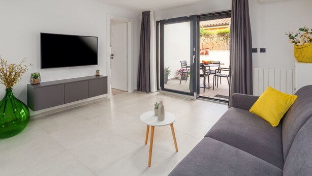 Un saló modern amb televisió de pantalla plana, un sofà gris i una taula blanca petita.