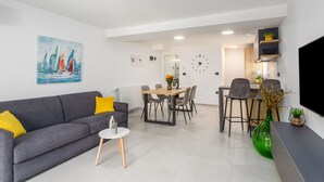 Un saló modern amb un sofà gris, una taula rodona petita i una zona de menjador amb taula i cadires de fusta.