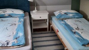 Ett litet, enkelt rum med två enkelsängar, ett nattduksbord med en lampa och en randig matta.