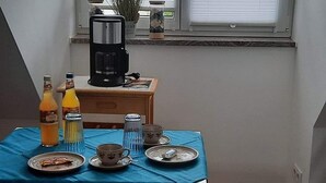 Ett litet matområde med ett bord för två personer, en kaffebryggare och ett fönster med persienner.