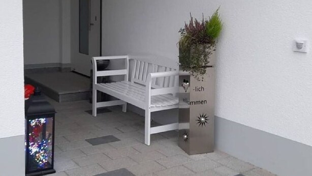 En vit bänk utanför en byggnad med en skylt som visar texten: ”Lägenhet Maria Waldblick”.