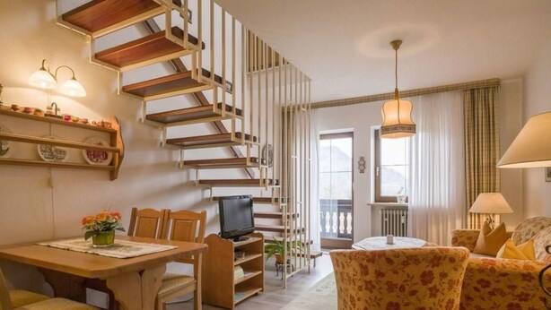 Een gezellige woonkamer met een houten trap, een eethoek en een bank.