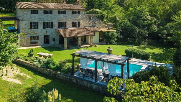 Une villa en pierre dotée d’une piscine, entourée d’une végétation luxuriante et sous un ciel dégagé.