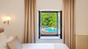 Une chambre d’hôtel avec un lit, une fenêtre avec des rideaux, une vue sur une piscine et un luminaire fixé au mur.