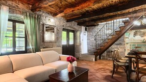 Un salon chaleureux avec un canapé, une table basse en bois et un coin repas comprenant des chaises et une table. Un escalier avec une rampe en bois mène à l’étage supérieur.