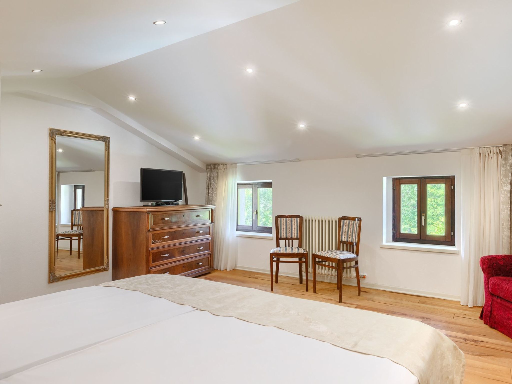Un dormitorio con cama, cómoda, televisión, dos sillas y ventana.