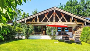Ein rustikales Holzhaus mit überdachter Terrasse, Sitzgelegenheiten im Freien und einem gepflegten Rasen.