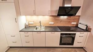Eine moderne Küche mit Spüle aus Edelstahl, Holzrückwand und eingebautem Backofen.