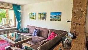Ein Wohnzimmer mit einem braunen Sofa, einem Glastisch und drei Landschaftsbildern an der Wand.