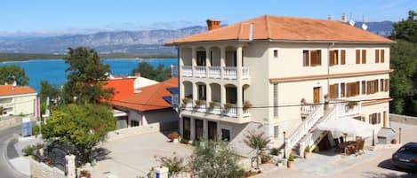 Ein zweistöckiges Gebäude mit einem Balkon, einer Steinmauer und Blick auf das Meer.
