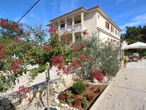 Ein zweistöckiges Gebäude mit Balkon, umgeben von einem Garten mit verschiedenen Pflanzen und Blumen.