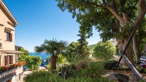 Edifici d'estil mediterrani amb façana de pedra, un balcó amb flors vermelles i vista al mar.