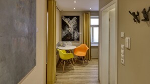 A hallway with a dining area featuring a white table and two orange chairs, a large abstract painting on the wall, and a door with a light switch and thermostat. - Gäuls-Stadl by Interhome (Marktheidenfeld)