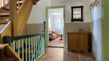 Eine Holztreppe mit grüner Handlauf, die zu einem Raum führt, der mit gemustertem Wandpapier, einem Holzschrank und einem gerahmten Bild dekoriert ist.