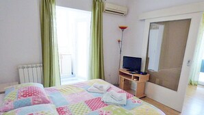 Un dormitorio con una cama grande, un televisor sobre un soporte y una puerta corrediza que da a un balcón.