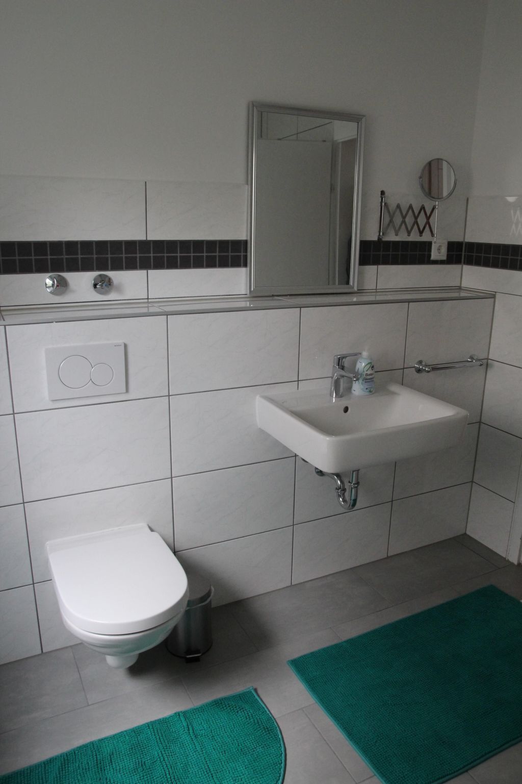 A bathroom with a white toilet, a sink, a mirror, and a trash bin.