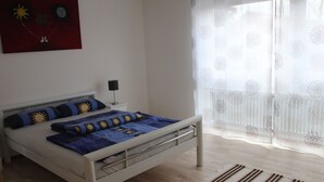 A bedroom with a bed, a nightstand, a lamp, a window with sheer curtains, and a painting on the wall. - Wunderschön Wohnen in Weinheim by Interhome (Weinheim)