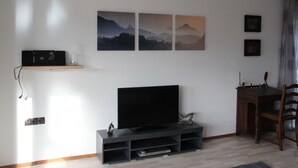 A modern living room with a flat-screen TV, a wooden dining table, and three framed pictures on the wall. - Wunderschön Wohnen in Weinheim by Interhome (Weinheim)