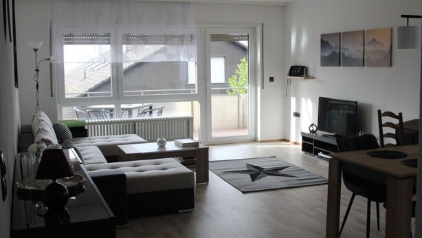 A modern living room with a sofa, a coffee table, and a TV. There is a dining area with a table and chairs. The room has large windows and a view of the outside. - Wunderschön Wohnen in Weinheim by Interhome (Weinheim)