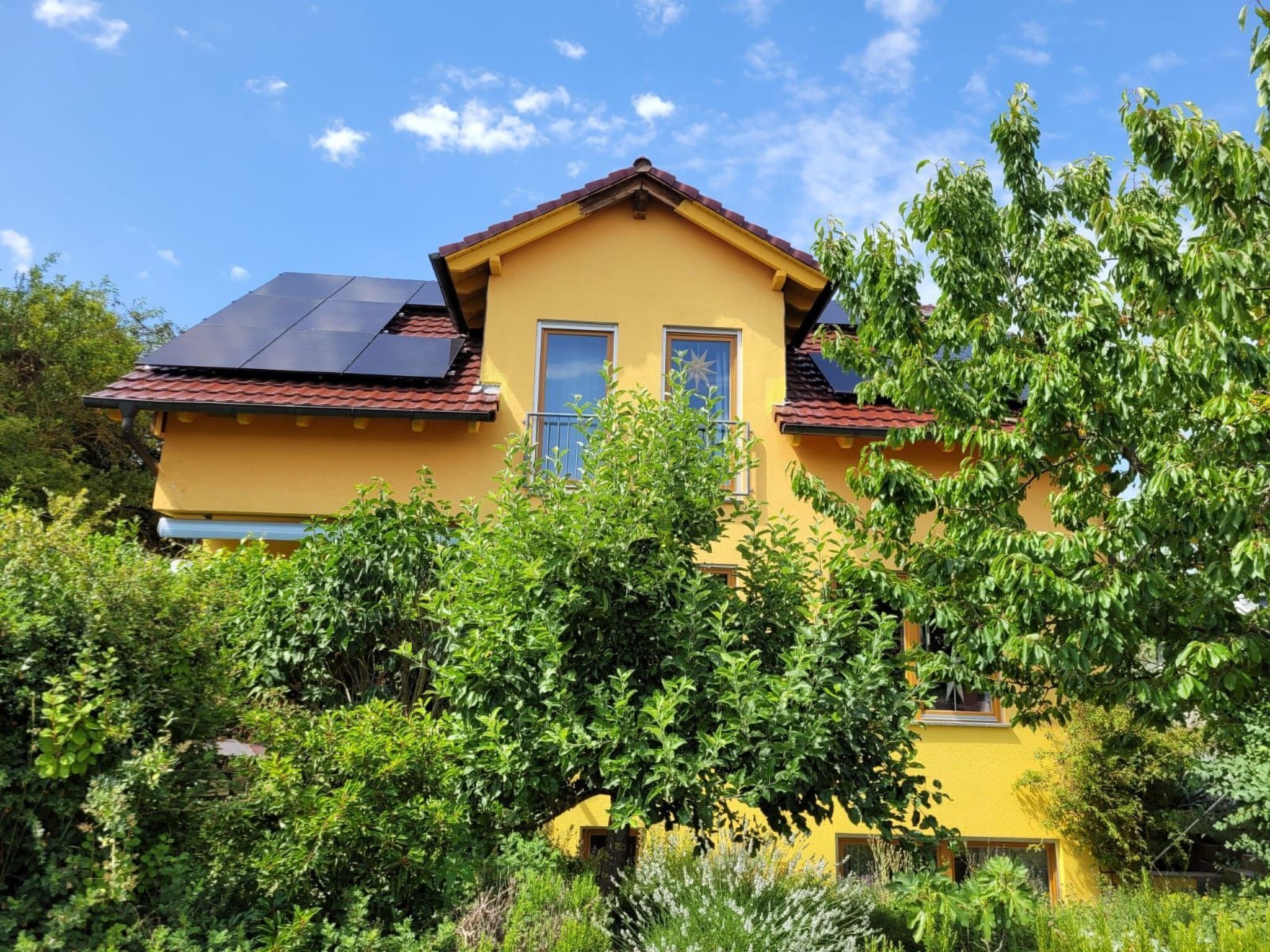 Ein gelbes Haus mit rotem Dach, umgeben von üppigem Grün.