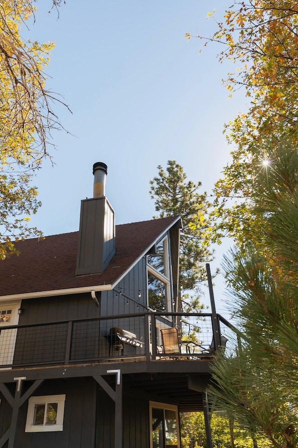 A two-story building with a visible chimney, a balcony with a grill, and a window on the lower level.