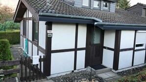 Ein zweistöckiges Haus mit dunkelbraun-weißer Fassade, einem Ziegeldach und einem kleinen Garten mit Holzzaun.