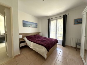 Ein Schlafzimmer mit einem Bett, einem fensterförmigen Ausblick mit Vorhängen, einem Heizkörper und einem Bild an der Wand.