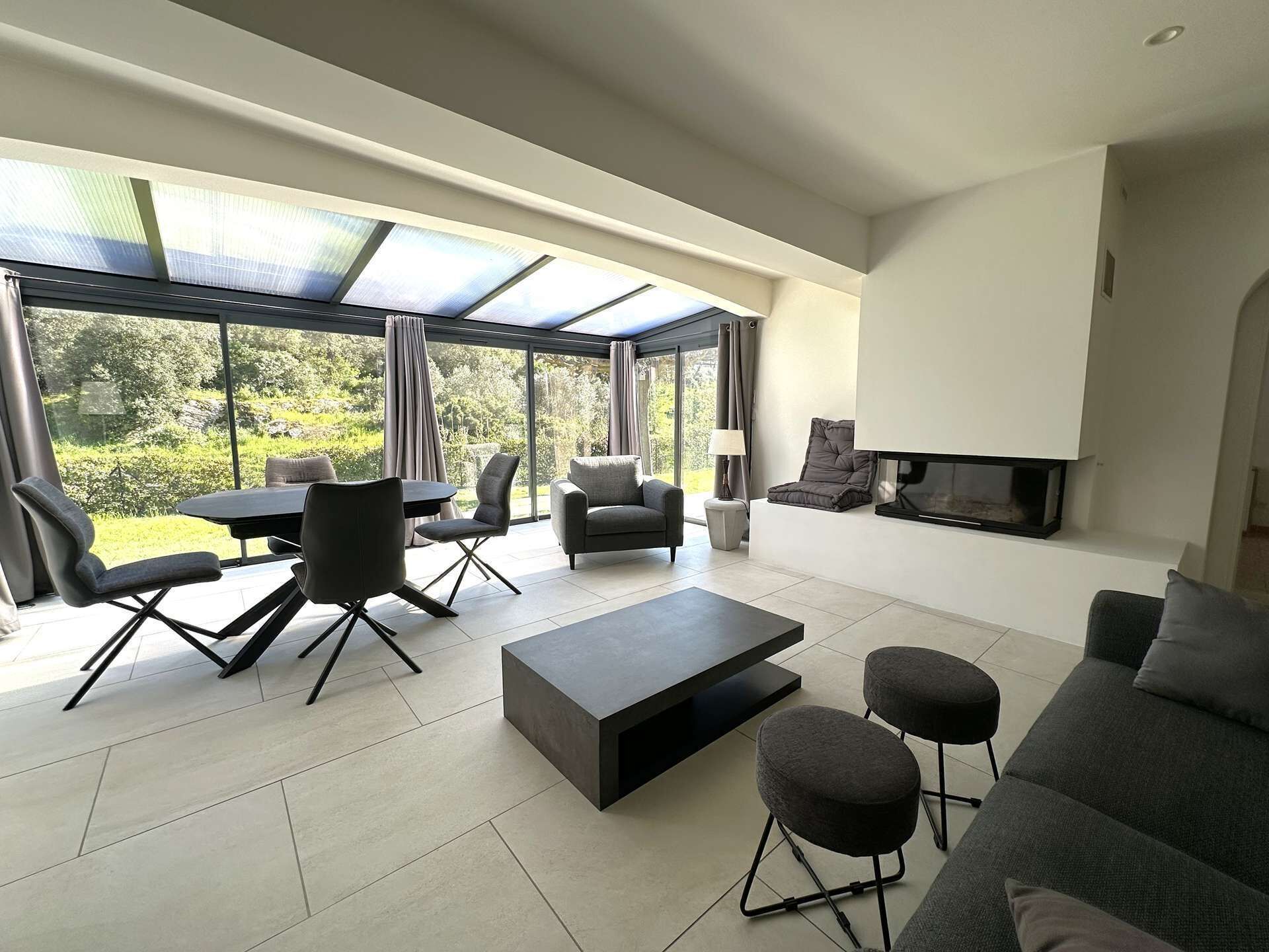 A modern living room with a glass ceiling, a fireplace, and a view of greenery.
