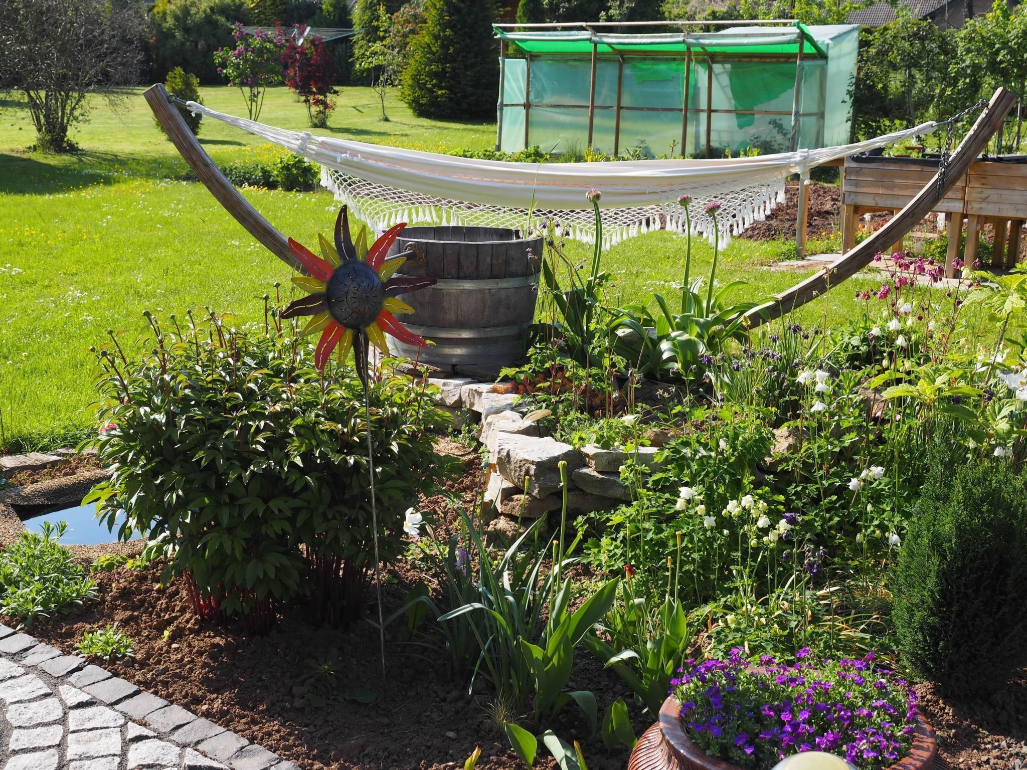 A garden with a hammock, a decorative metal flower, and various plants.