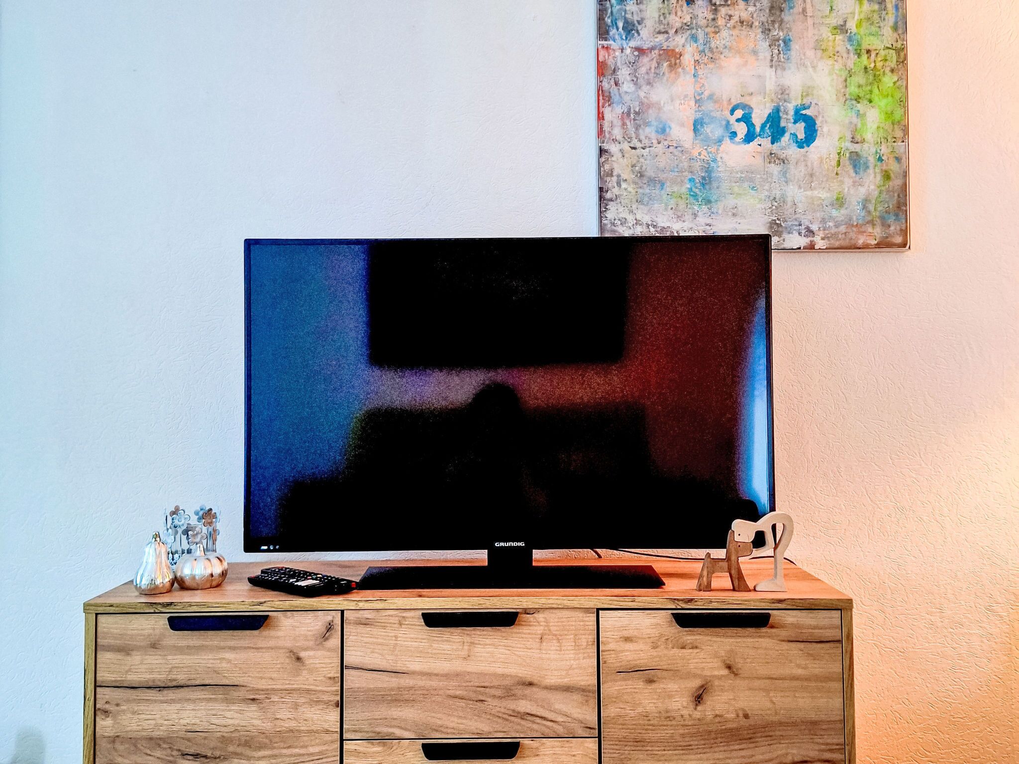 En tv-apparat placerad på ett träskåp, tillsammans med en fjärrkontroll och dekorativa föremål.