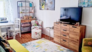 Een woonkamer met een televisie, een houten kast, een fauteuil met bloemenprint en een kleine ronde tafel.