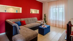 A living room with a red wall, a grey sofa, a blue ottoman, and a television. - Haus Mia by Interhome (Labin)