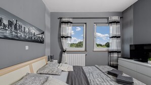 A modern bedroom with a bed, two windows, a TV, and a cityscape painting. - mit Blick auf das Wasser by Interhome (Labin)