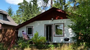 Una casita de techo rojo y paredes blancas, rodeada de follaje.