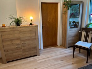 Una habitación con un armario de madera, una silla, una puerta y una ventana con plantas.