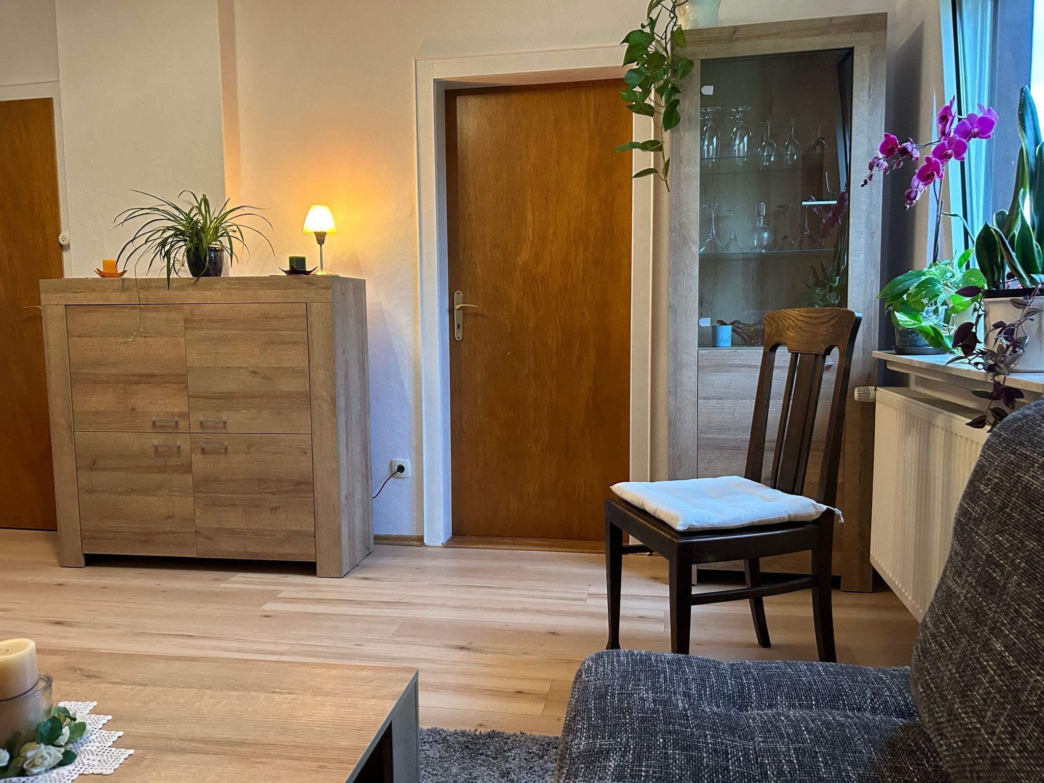 A living room with a wooden cabinet, a chair, a table with a candle, and a potted plant.