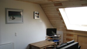 A cozy room with a sloped ceiling, a wooden table, a black sofa, and a television on a shelf. - Appartement in Steinhude mit Grill by Interhome (Wunstorf)
