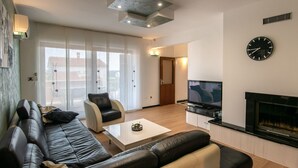 Un salon moderne avec un canapé en cuir noir, une table basse et un téléviseur fixé au mur.