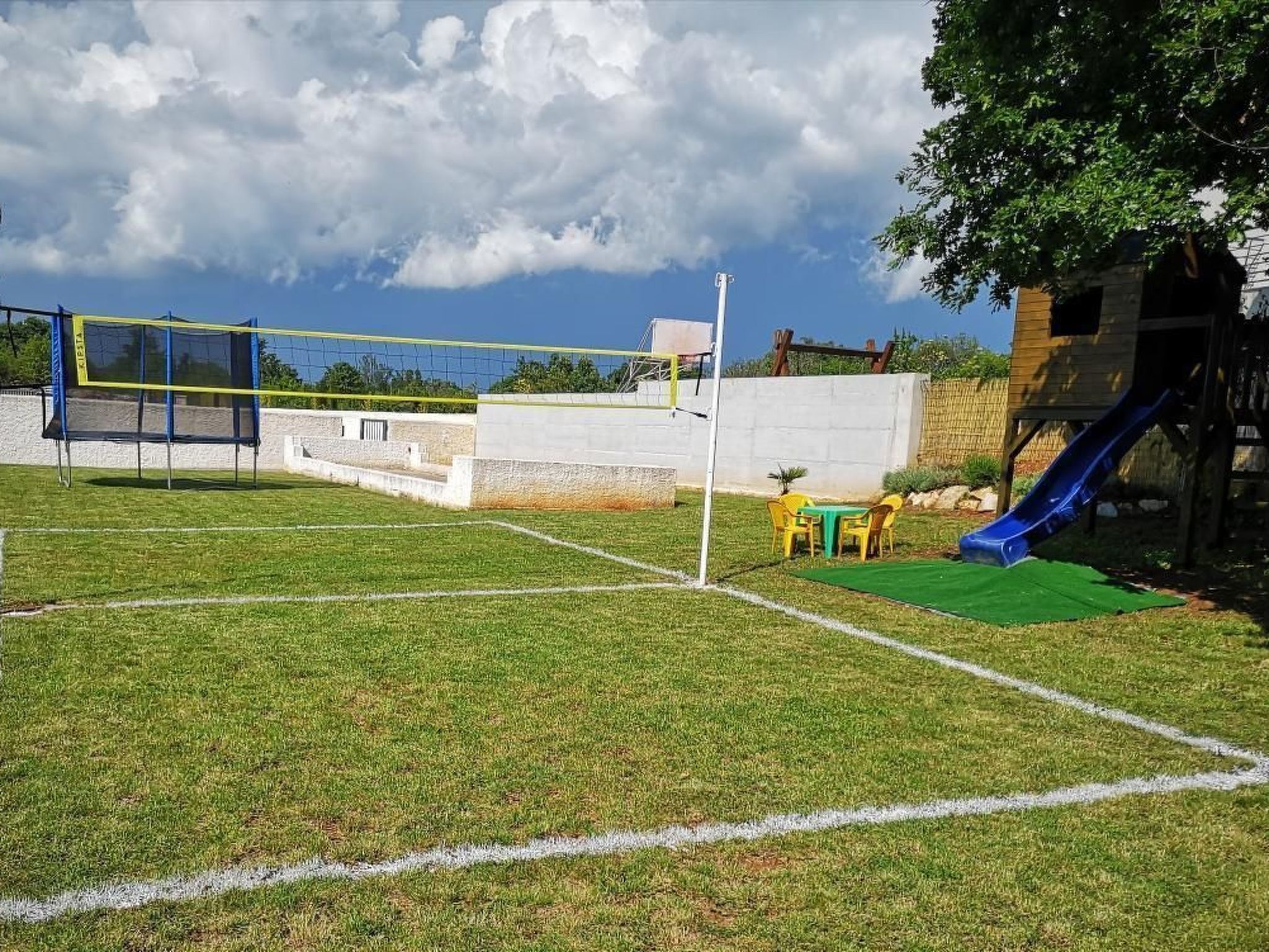 Un espacio al aire libre con césped, una red de voleibol, un tobogán y una pequeña mesa con sillas.