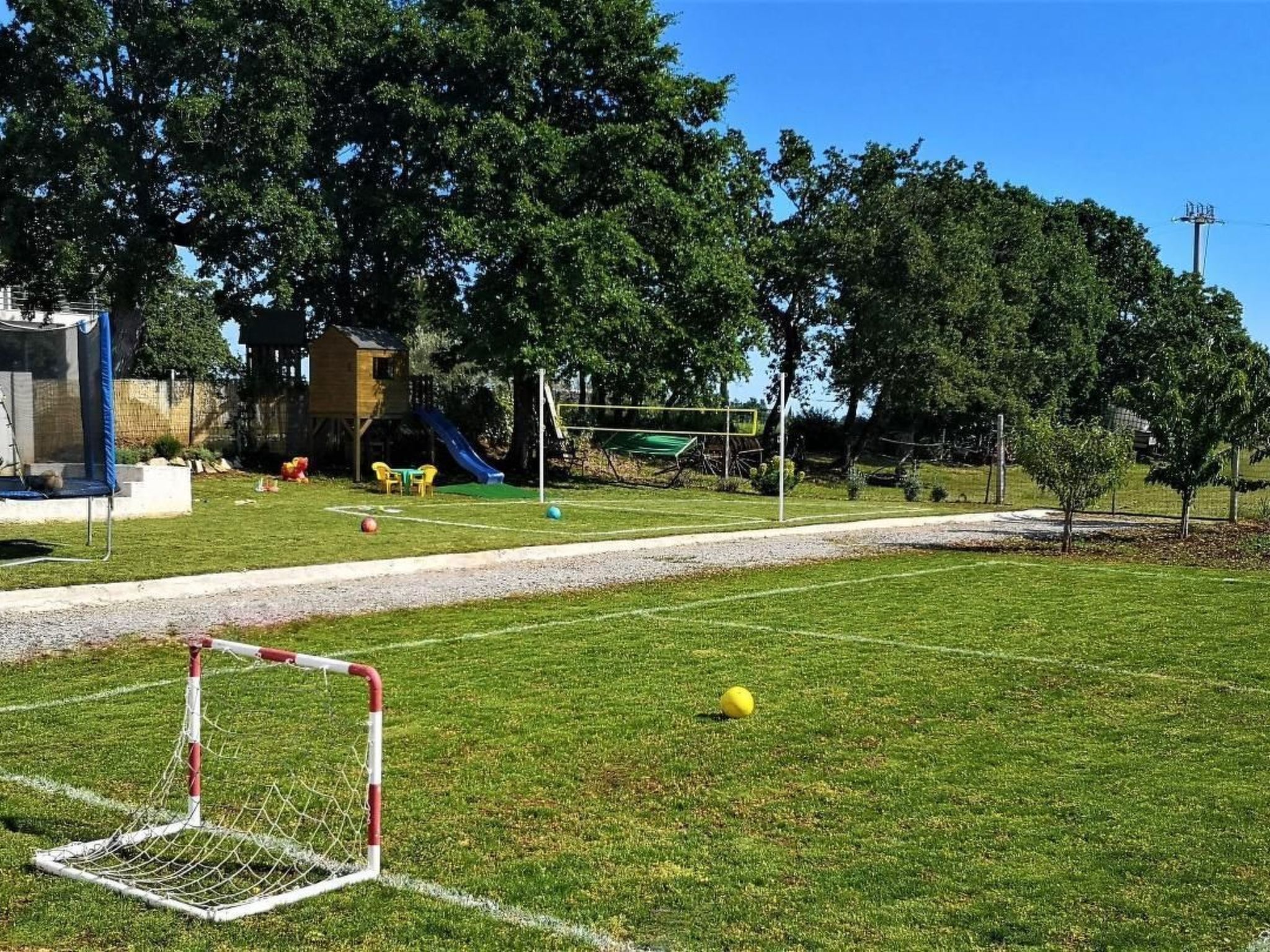 Un champ d’herbe avec un but de football, une aire de jeux avec un toboggan et des arbres en arrière-plan.
