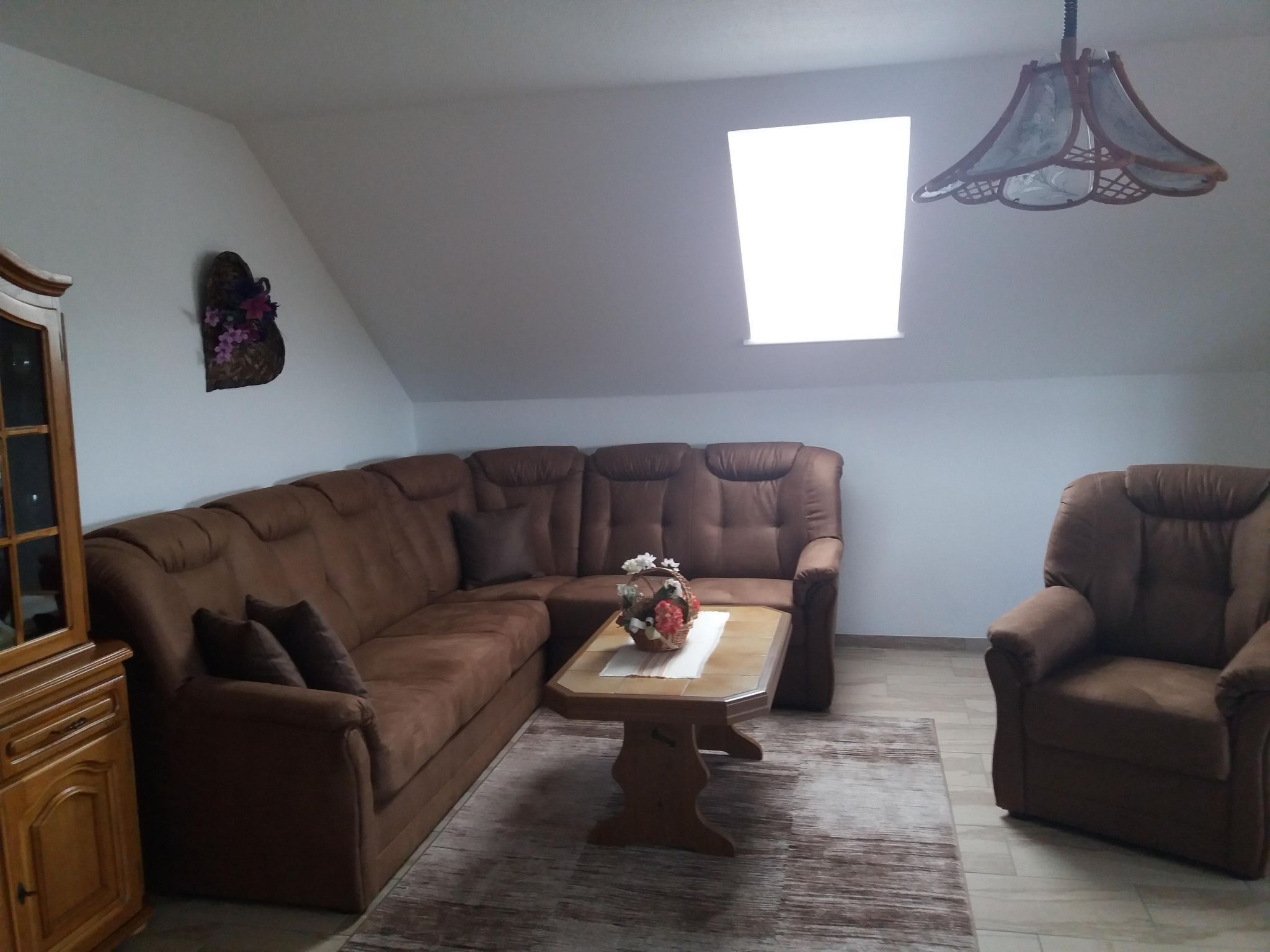 Una sala de estar con un sofá seccional marrón, una mesa de centro de madera, un sillón marrón y una ventana con luz natural.