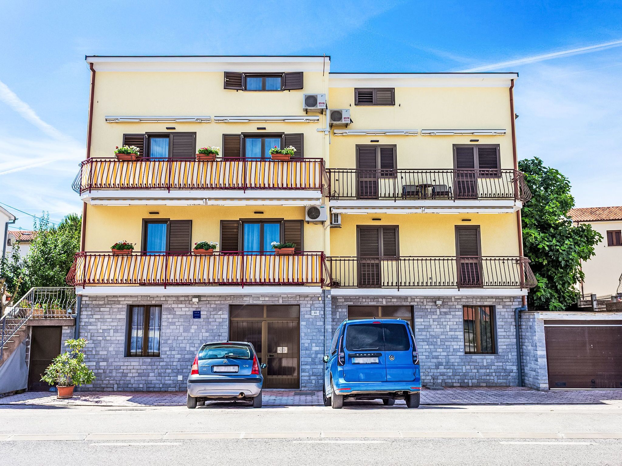 Ein zweistöckiges Gebäude mit Garage, ein Auto vor der Tür und einem Blumentopf auf dem Bürgersteig.