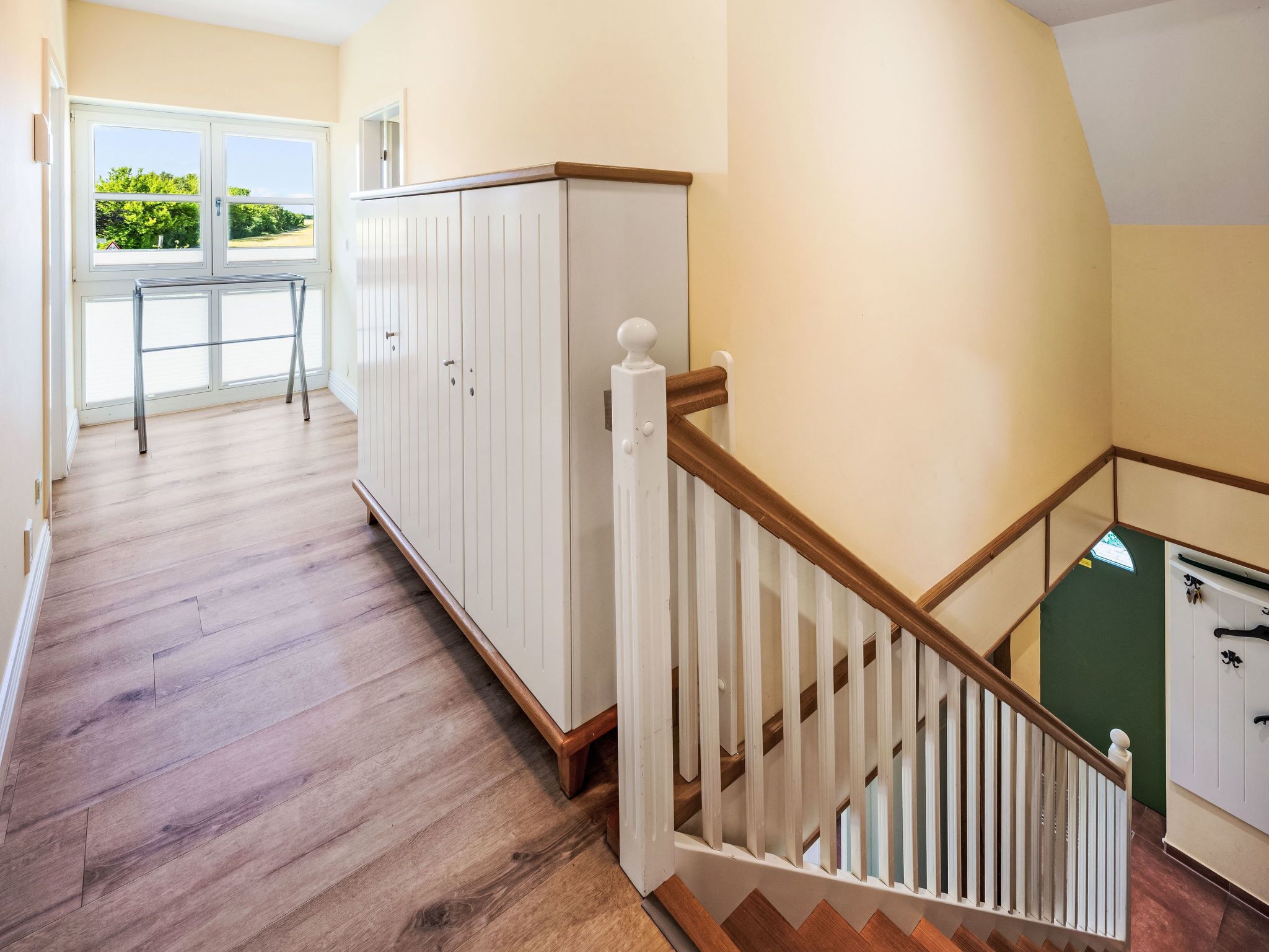 A hallway with wooden flooring, white cabinets, and a staircase with a wooden railing.