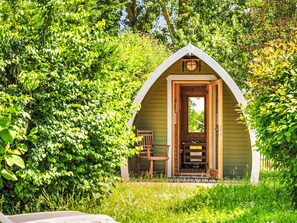A small, green, A-frame structure with a wooden bench and a door, surrounded by lush greenery. - Reethaus Mertinat ''For Six'' mit Meerblick by Interhome (Gollwitz (Insel Poel))