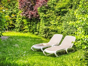 Due poltrone in un rigoglioso giardino con diverse piante e un tavolino con una tazza e un libro.
