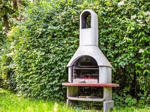 A concrete outdoor grill with a chimney, set against a backdrop of dense green foliage. - Reethaus Mertinat ''For Six'' mit Meerblick by Interhome (Gollwitz (Insel Poel))