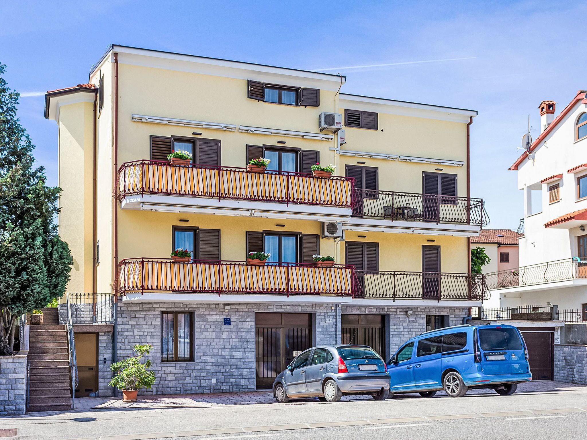 Un immeuble à plusieurs étages doté de balcons, d’un abri pour voitures et d’un petit jardin.