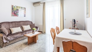 Ein Wohnzimmer mit einer Couch, einem Holztisch, einem Esstisch mit Stühlen, einem Heizkörper und einer Klimaanlage.