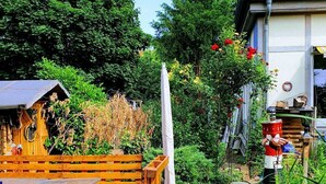 En træterrasse med et bord og stole, omgivet af frodig vegetation og en have.