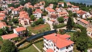 An aerial view of a residential area with red-tiled roofs, a central green space, and a body of water in the background. - Villa Liet 9. by Interhome (Poreč/Funtana)
